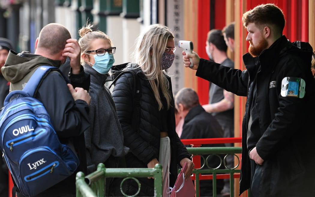 A security guard uses a handheld thermometer to take the temperature of customers,  as they wait to enter a bar in Liverpool, north west England on October 2, 2020, following the  announcement of new local restrictions in the northwest