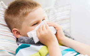childhood, healthcare and medicine concept - ill boy with flu blowing nose at home