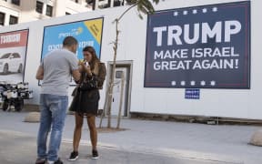 Two people stand in front of a 'Trump make Israel great again!' sign in Israel