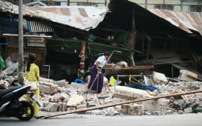 A woman clears debris in front of damaged houses in Mandalay on March 30, 2025, two days after an earthquake struck central Myanmar. The death toll from a huge earthquake that hit Myanmar and Thailand passed 1,600, as rescuers dig through the rubble of collapsed buildings in a desperate search for survivors. The quake destroyed buildings, downed bridges and buckled roads across swathes of Myanmar, with massive destruction seen in Mandalay. (Photo by Sai Aung MAIN / AFP)