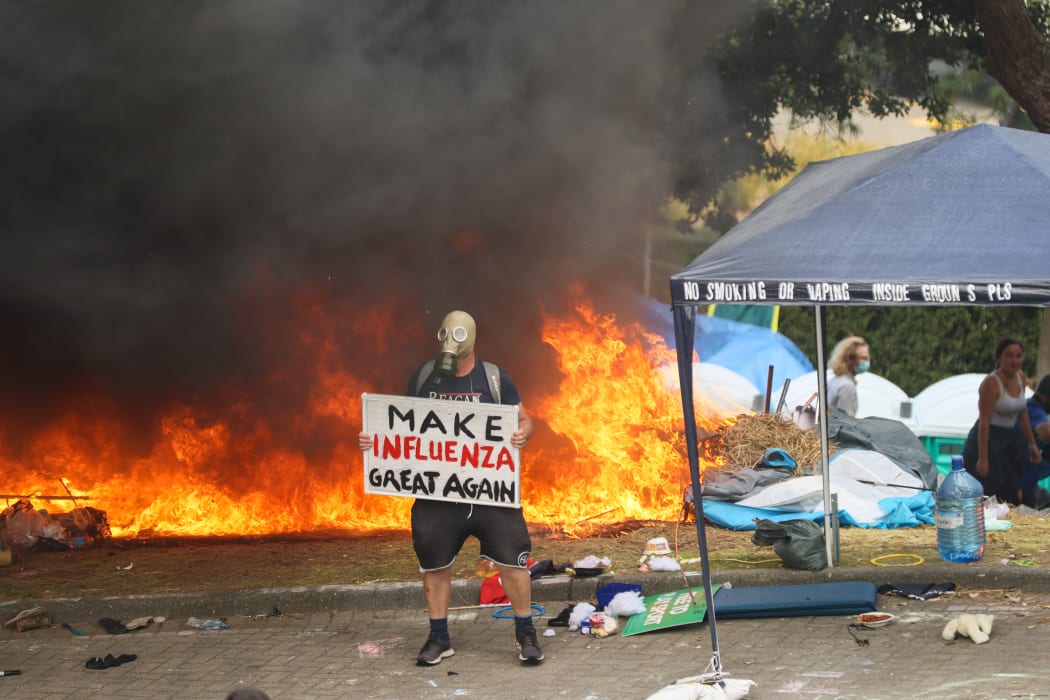 A protest stands in front a fire with a puzzling sign.