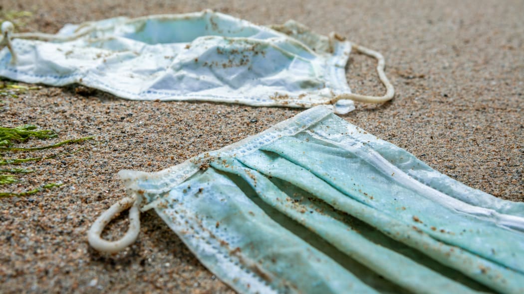 Green medical mask waste during COVID19. Discarded to ocean coronavirus single-use face masks. Environmental and coast plastic pollution. Trash in beach threatening the health of oceans