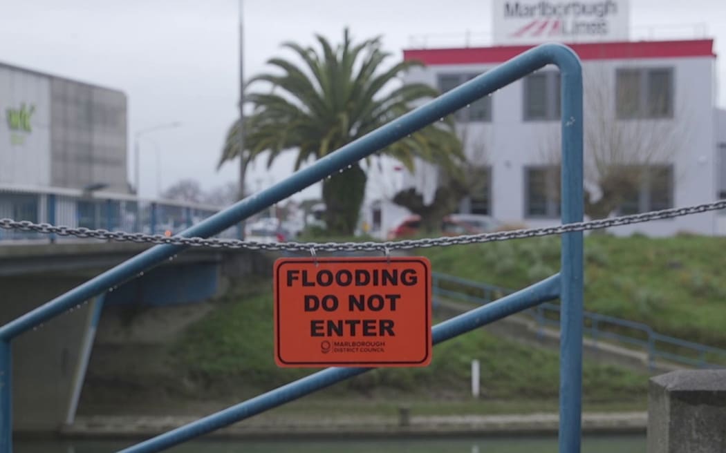 A flood warning sign hangs in front of a footpath to the Taylor River in central Blenheim