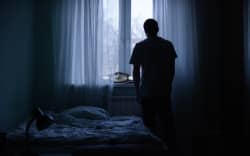 Alone man silhouette staring at the window closed with curtains in bedroom.
