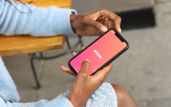 A woman holds a phone with the Tinder app open