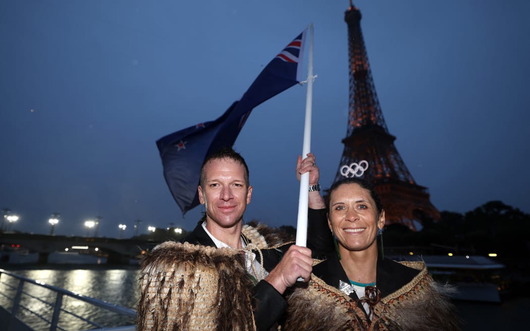 PARIS, FRANCE - JULY 26: Jo Aleh and Aaron Murray Gate, Flagbearers of Team New Zealand, look on with a Flag of Team New Zealand on a boat on the River Seine during the opening ceremony of the Olympic Games Paris 2024 on July 26, 2024 in Paris, France. (Photo by Hannah Peters / POOL / AFP)