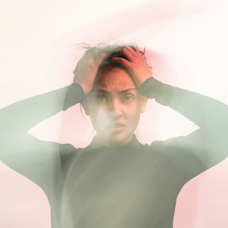 A woman in soft focus holds her hands to her head and frowns.