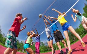 Teenagers playing volleyball together outside on a sunny day.