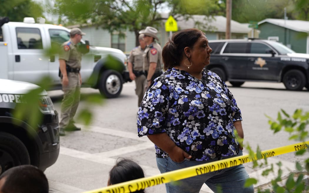 People sit on the curb outside of Robb Elementary School as State troopers guard the area in Uvalde, Texas, on May 24, 2022. - An 18-year-old gunman killed 14 children and a teacher at an elementary school in Texas on Tuesday, according to the state's governor, in the nation's deadliest school shooting in years. (Photo by allison dinner / AFP)