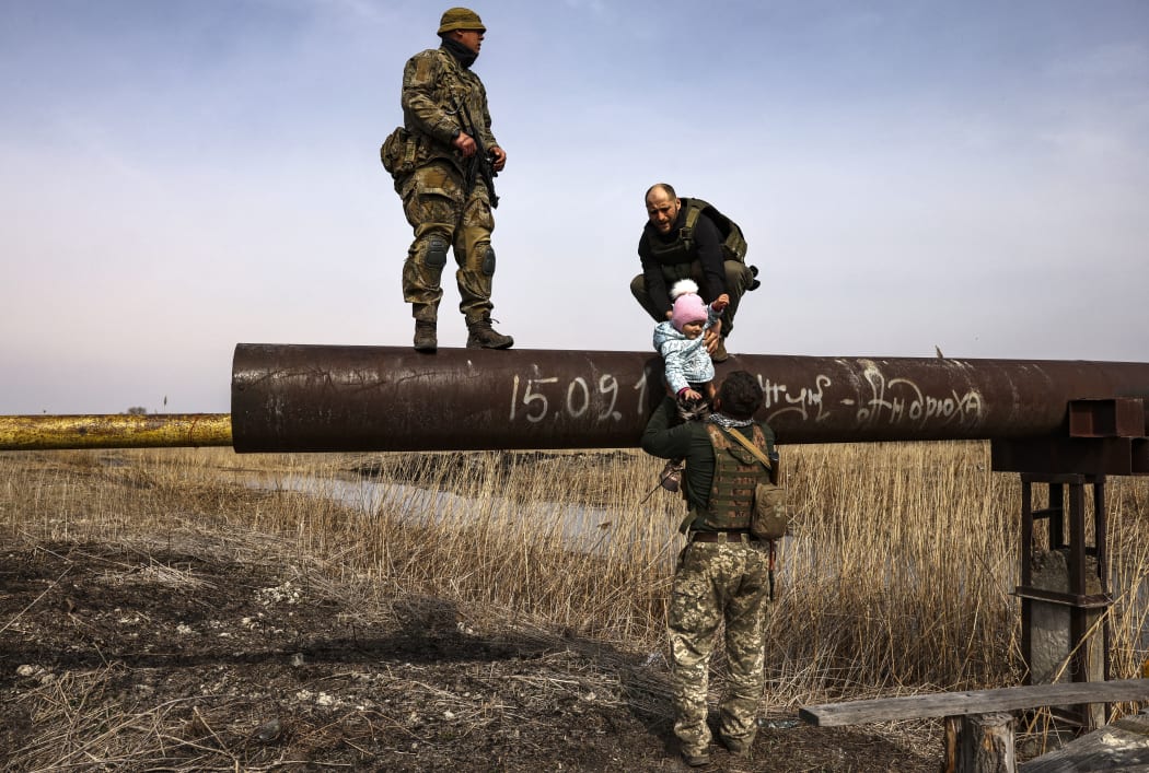 Ukrainian serviceman Andriy (right) hands over the baby of a displaced family to help to cross a river, on the outskirts of Kyiv, on 31 March, 2022.
