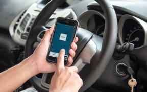 A man hand holding screenshot of Uber app in a car.