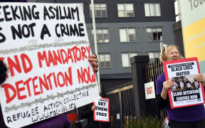People hold up placards during a pro-refugee rights protest in Melbourne on June 13, 2020 as several asylum seekers who were evacuated for medical reasons from offshore detention centres on Nauru and Manus Island, look down from the hotel where they have been detained.