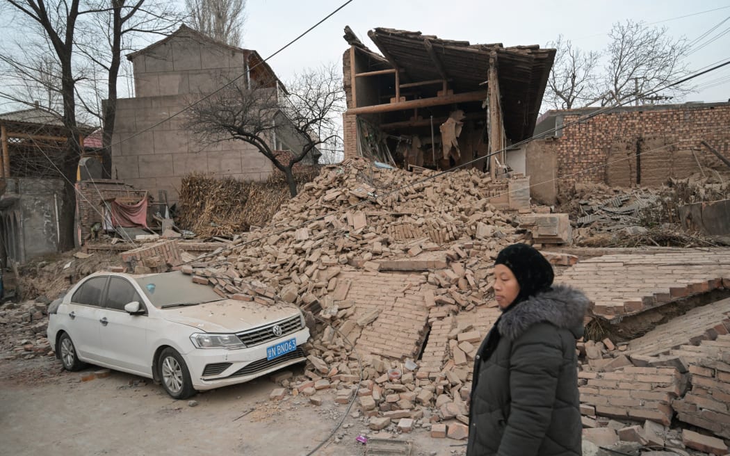 A woman walks past a collapsed house in Dahejia in Jishishan County in northwest China's Gansu province on December 20, 2023. Survivors of China's deadliest earthquake in years huddled in aid tents on December 20 after overnight temperatures plunged well below zero, with the death toll rising to 131.