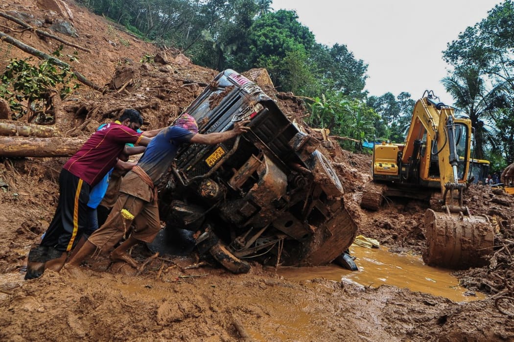 Rescue workers push a overturned vehicle stuck in the mud and debris at a site of a landslide  caused by heavy rains in Kokkayar in India's Kerala state on October 17, 2021.