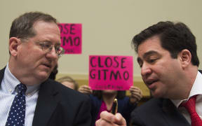 Demonstrators hold up placards as US Department of State Special Envoy for Guantanamo Closure Lee Wolosky and US Department of Defense Special Envoy for Guantanamo Closure Paul Lewis testify before the House Foreign Affairs Committee.