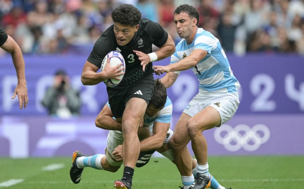 New Zealand's Tone Ng Shiu is tackled by Argentina's Santiago Alvarez and Argentina's Joaquin Pellandini (R) during the men's placing 5-8 rugby sevens match between New-Zealand and Argentina during the Paris 2024 Olympic Games at the Stade de France in Saint-Denis on July 27, 2024. (Photo by CARL DE SOUZA / AFP)