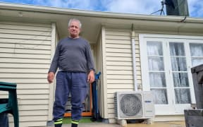 Steven Schaunkel stands in front of his house wearing a grey long sleeve top, blue pants and black and bright yellow socks.