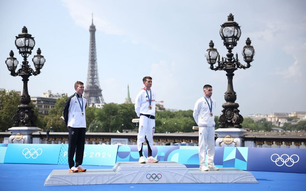 Gold medallist Britain's Alex Yee (C), silver medallist New Zealand's Hayden Wilde and bronze medallist France's Leo Bergere stand on the podium during the victory ceremony for the men's individual triathlon at the Paris 2024 Olympic Games in central Paris on July 31, 2024. (Photo by Anne-Christine POUJOULAT / AFP)