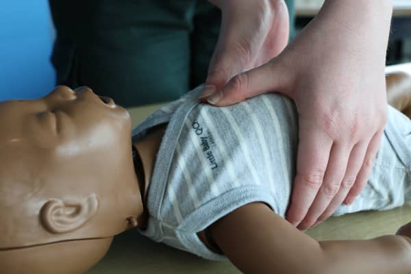St John’s Three Steps for Life delivery lead Mia Noyes performing chest compression using her thumbs for CPR on an infant manikin.