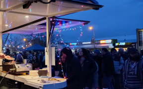 A bustling market at twilight. A food truck strung with fairy lights is busy making orders.