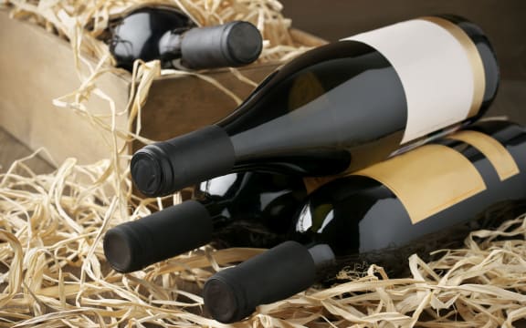 Assorted closed wine bottles lying on straw and vintage wooden box.