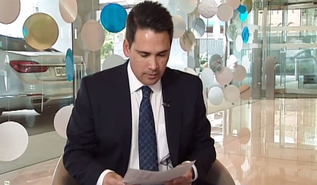 Simon Bridges looks at Newshub;s leaked list of his travel expenses during Monday's exclusive report  - with his crown car in the background.