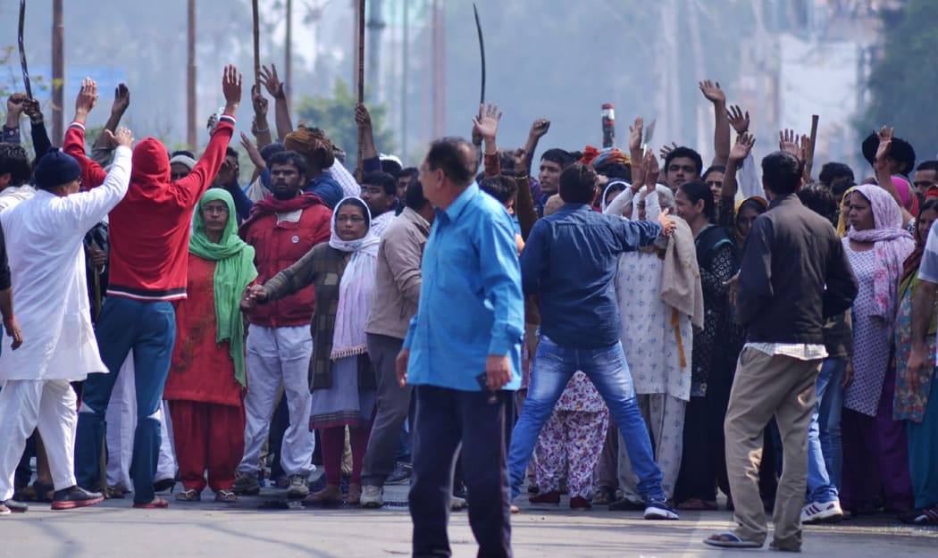 Indian residents gather on a street as others gesture to hold them back amid ongoing caste protests in Rohtak