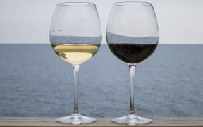 Glasses of wine - one white, one red - against a backdrop of a lake or the sea.