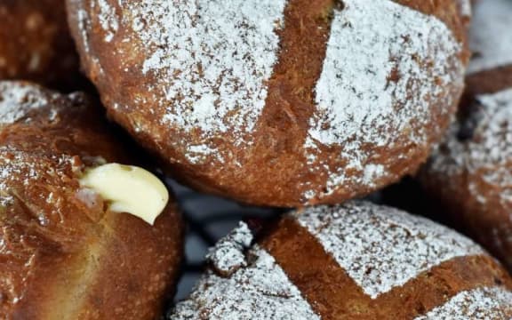 An icing sugar-dusted round doughnut, with a stencilled cross pattern on top, balanced on several other doughnuts.
