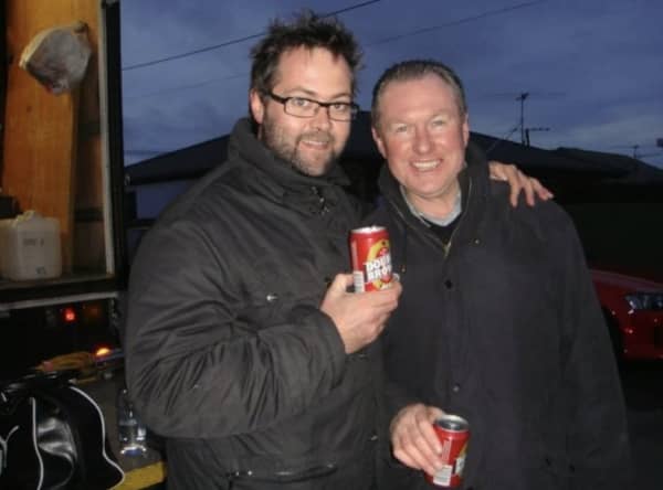 Scotty Stevenson and Stu Wilson stand outside at dusk smiling and holding cans of beer.