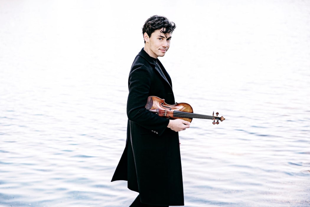 Violinist Benjamin Beilman carrying his violin beside calm water
