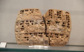 An ancient clay tablet which has split into two, displayed at a museum. The photo is close up to the artifact.