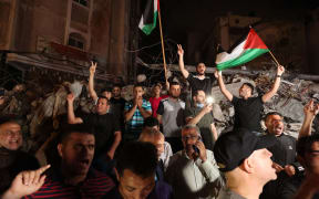 A man waves the Palestinian flag as others flash the V-sign for victory as they celebrates in front of a destroyed building the ceasefire brokered by Egypt between Israel and the two main Palestinian armed groups in Gaza on 20 May 2021.