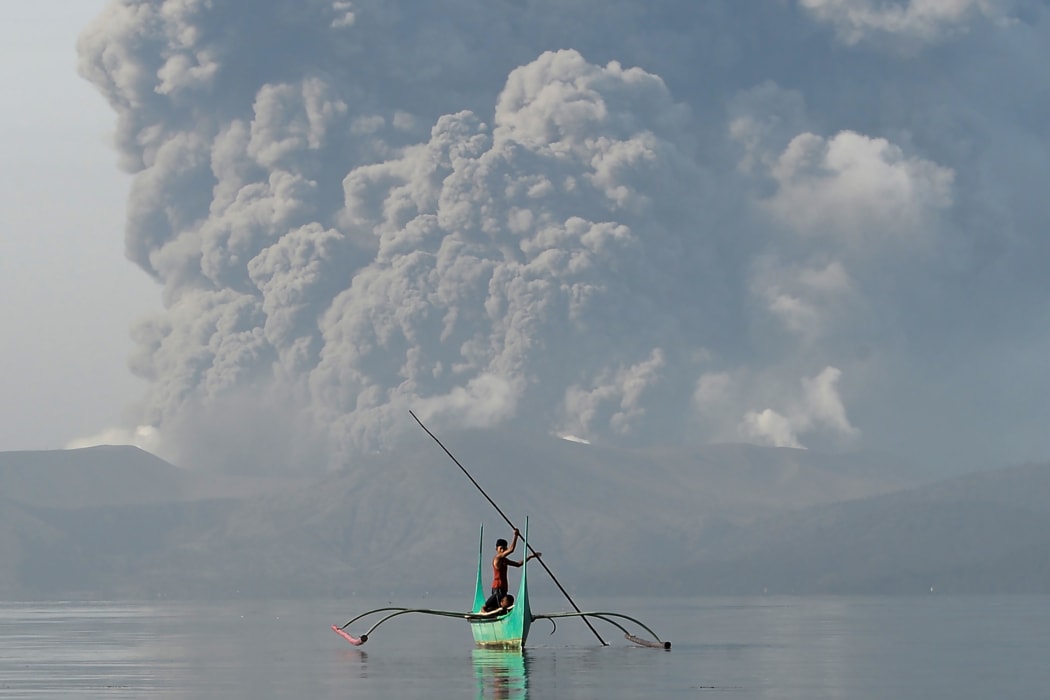 A youth living at the foot of Taal volcano rides an outrigger canoe while the volcano spews ash as seen from Tanauan town in Batangas province, south of Manila, on January 13, 2020.