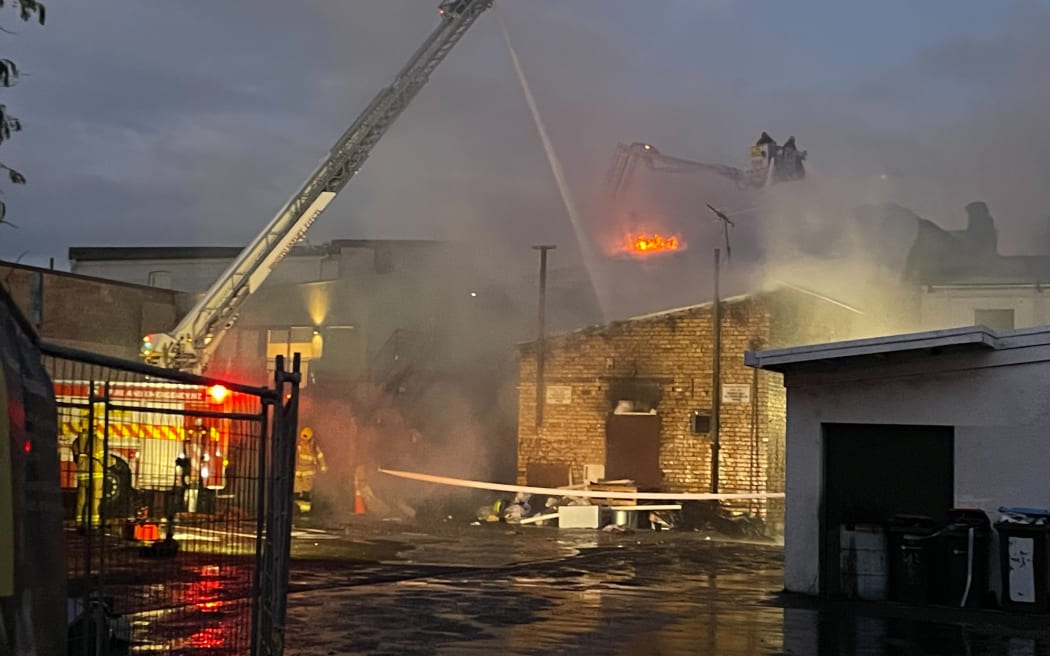 Flames could be seen over the top of a building in Onehunga Mall Road, as firefighters work from ladders, on Sunday night, 25 January, 2026.