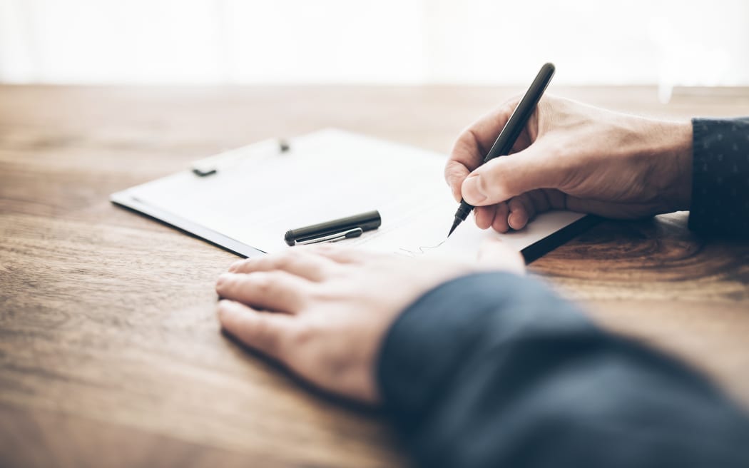 close-up shot of businessman signing contract or document on wooden desk