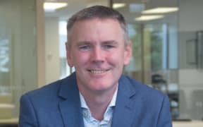 This is a head shot of Greame Ward. He is wearing a blue suit and sat in what looks like a meeting room.