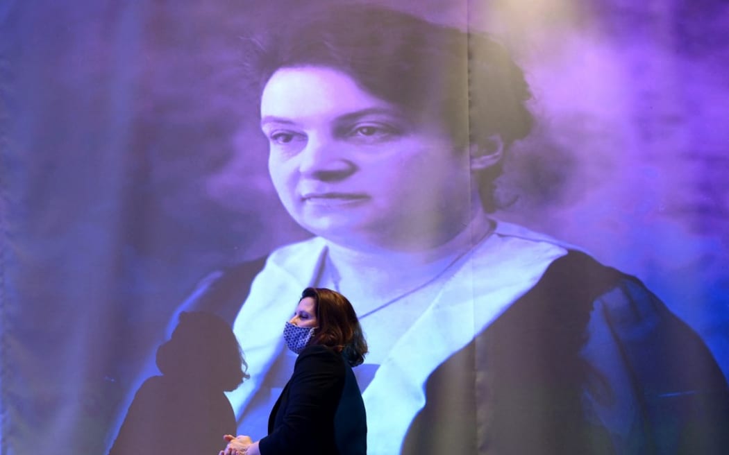 French Junior Sports Minister Roxana Maracineanu passes in front of a portrait of French athlete and pioneer of women's sports, Alice Milliat, during the inauguration of a statue in tribute to Milliat at the Maison du sport francais (French House of Sports), the headquarters of the French National Olympic and Sports Committee (Comite national olympique et sportif francais, CNOSF) in Paris on March 8, 2021. (Photo by FRANCK FIFE / AFP)