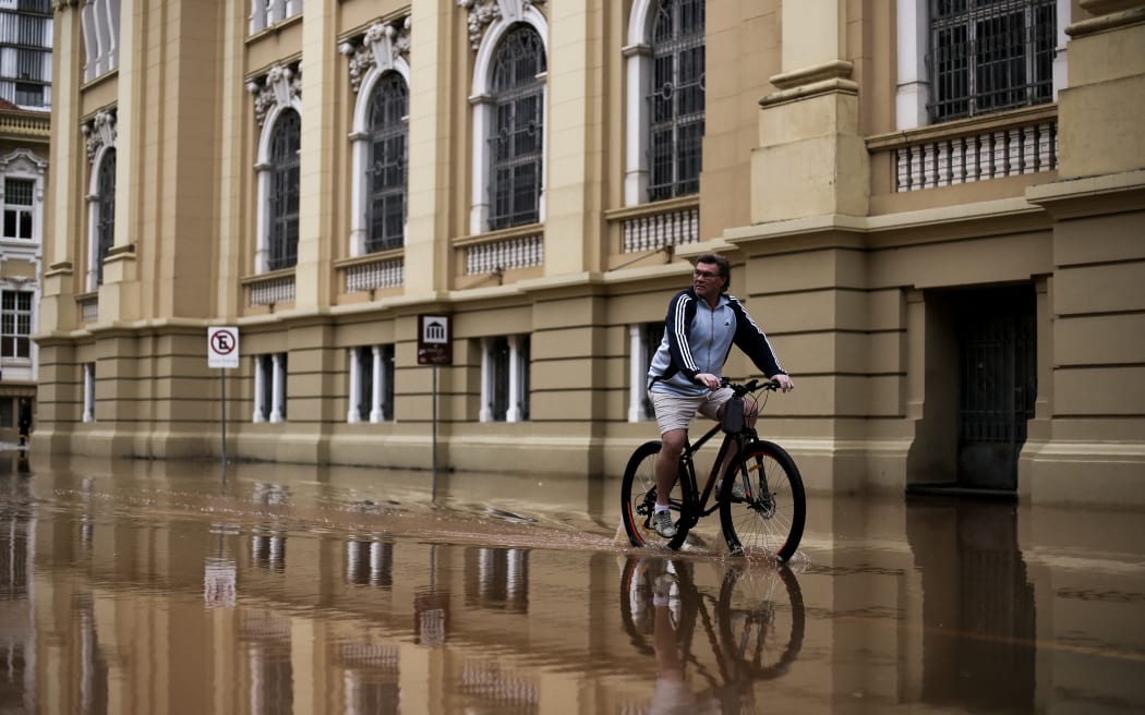 A man rides a bicycle in a flooded street at the historical center of Porto Alegre, Rio Grande do Sul state, Brazil on May 3, 2024. Brazilian President Luiz Inacio Lula da Silva on Thursday visited the country's south where floods and mudslides caused by torrential rains have killed 29 people, with the toll expected to rise. (Photo by Anselmo Cunha / AFP)
