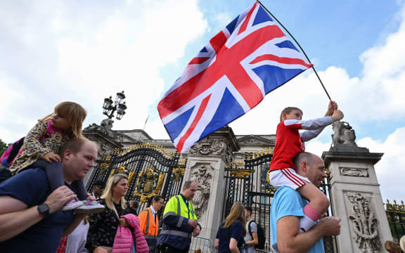 A boy waves a Britain national flag as others gather outside of Buckingham Palace in London on September 11, 2022. - Queen Elizabeth II's coffin will travel by road through Scottish towns and villages on Sunday as it begins its final journey from her beloved Scottish retreat of Balmoral. The Queen, who died on September 8, will be taken to the Palace of Holyroodhouse before lying at rest in St Giles' Cathedral, before travelling onwards to London for her funeral. (Photo by SEBASTIEN BOZON / AFP)