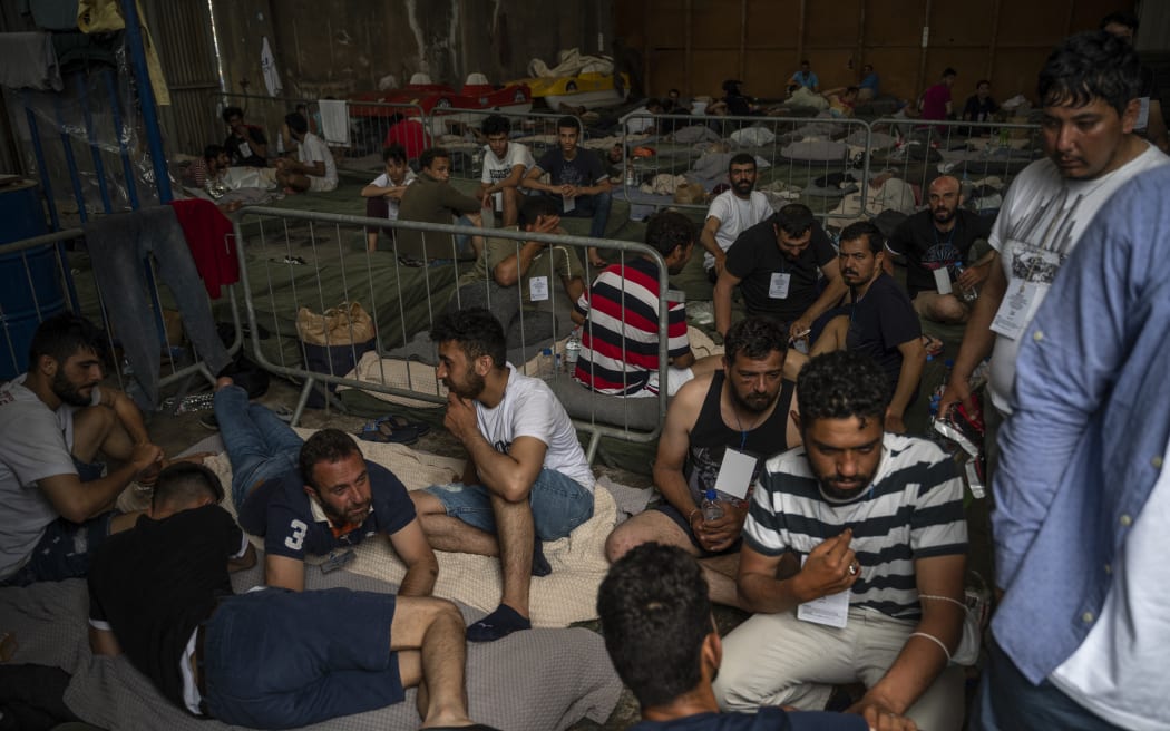 Survivors of a shipwreck sit inside a warehouse at the port in Kalamata town, on June 15, 2023, after a boat carrying migrants sank in international waters in the Ionian Sea. Greece has declared three days of mourning, the interim prime minister's office said on June 14, 2023, over a migrant boat sinking in the Ionian Sea feared to have claimed hundreds of lives. The Greek coastguard has so far recovered 79 bodies and rescued over 100, but survivors are claiming that up to 750 people were on board. (Photo by Angelos TZORTZINIS / POOL / AFP)
