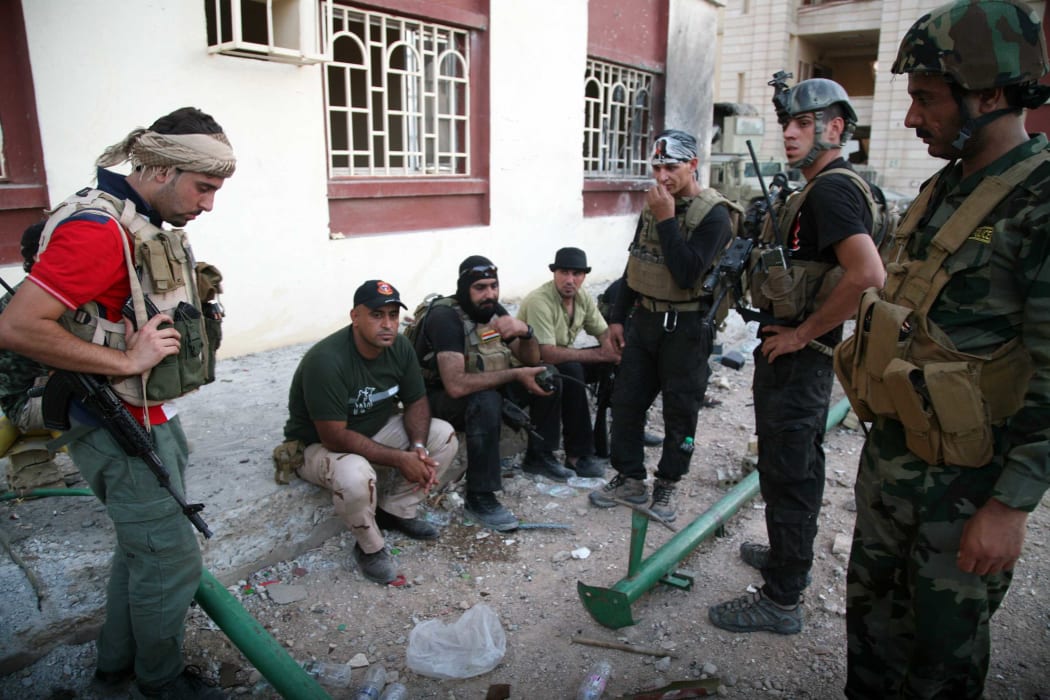 Iraqi security forces and gunmen rest on a sidewalk following clashes with jihadists in Ramadi, the capital of the western province of Anbar.