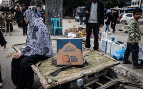 A Palestinian woman sits on a cart next to a box of food rations provided by US  charity World Central Kitchen at a makeshift street market in Rafah in the southern Gaza Strip on March 14, 2024, amid ongoing battles between Israel and the militant group Hamas. (Photo by MOHAMMED ABED / AFP)