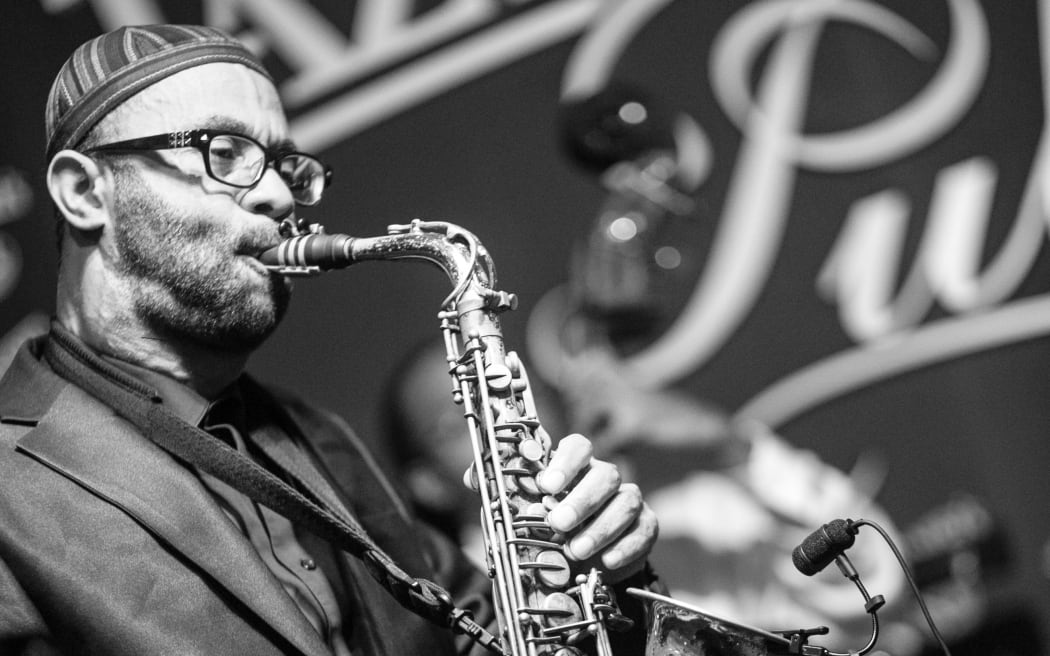 Kenny Garrett playing saxophone in front of a mural with the word "jazz" in it.