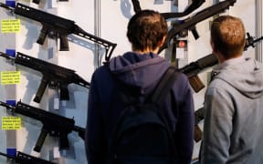 (FILES) In this file photo taken on March 29, 2019, visitors look at semi-automatic shotguns displayed on a wall during the 45th edition of the Arms Trade Fair, in Lucerne.