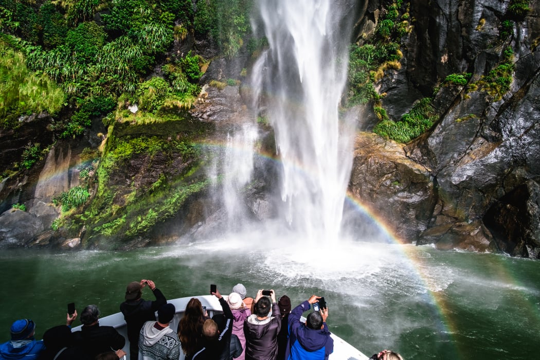 A group of tourists enjoying a stunning scene of nature while cruising into waterfall in Milford Sound, New Zealand.