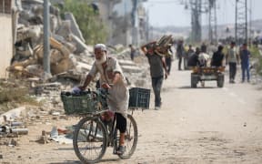 Displaced Palestinians at the Nuseirat refugee camp haul food parcels and other items they managed to get from a GHF aid distribution point at the so-called "Netzarim corridor" in the central Gaza Strip on July 26, 2025. (Photo by Eyad BABA / AFP)