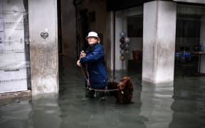 A woman walks her dog through a flooded street after an exceptional overnight "Alta Acqua" high tide water level, on 13 November, 2019 in Venice.