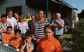 Tāneatua residents, including schoolchildren, gather outside the Tāneatua Police Station which was severely damaged in a fire nearly a year ago.