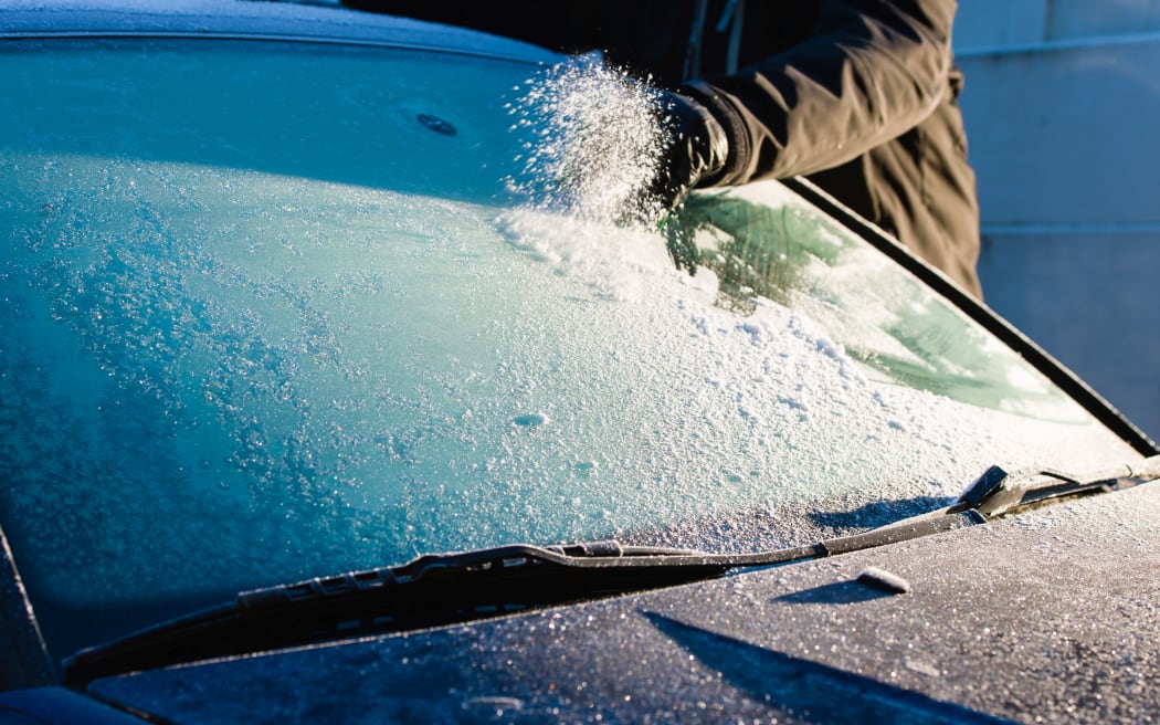 A man cleans frozen windshield by scratching, cold morning
